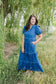 Woman in a blue dress standing in a field with greenery around