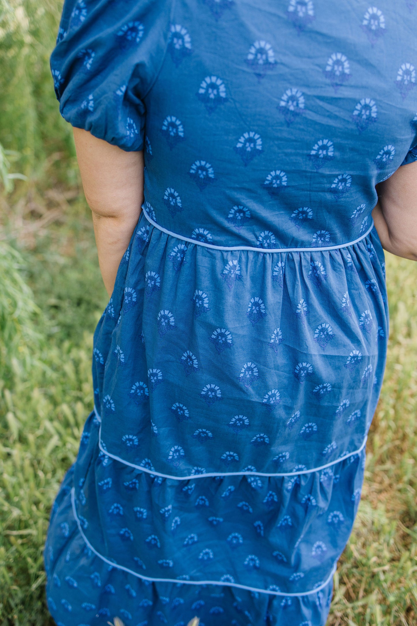 Person wearing a blue dress with white patterns standing in grass