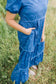Person wearing a blue dress with white patterns standing in a grassy field