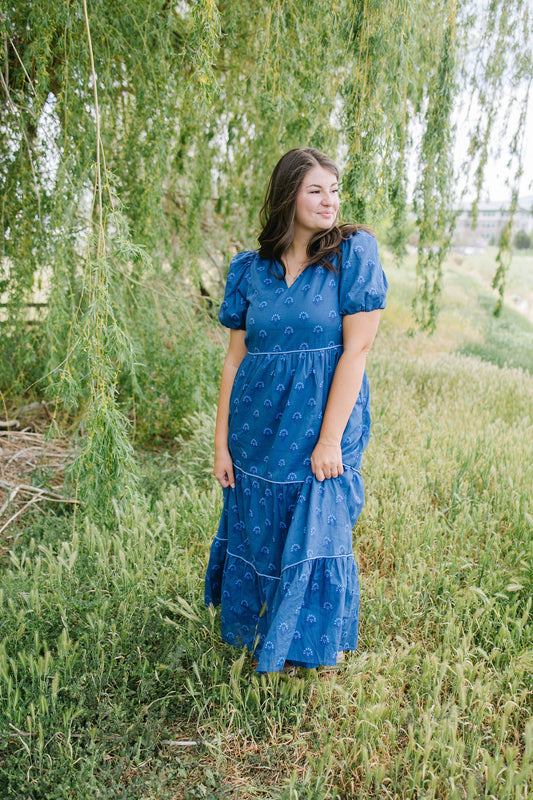 Woman in a blue dress standing in a field with a willow tree in the background