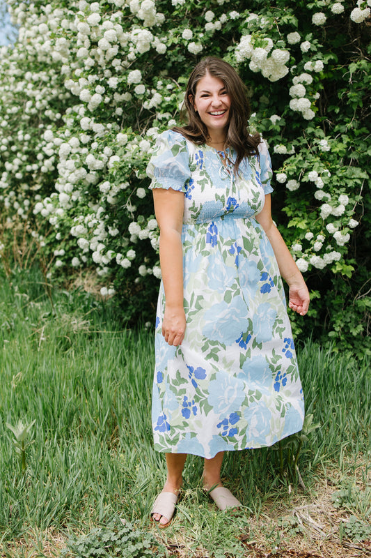 Woman in a floral dress standing in front of white flowers and greenery