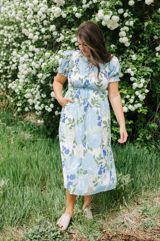 Woman in a floral dress standing in a garden with white flowers in the background