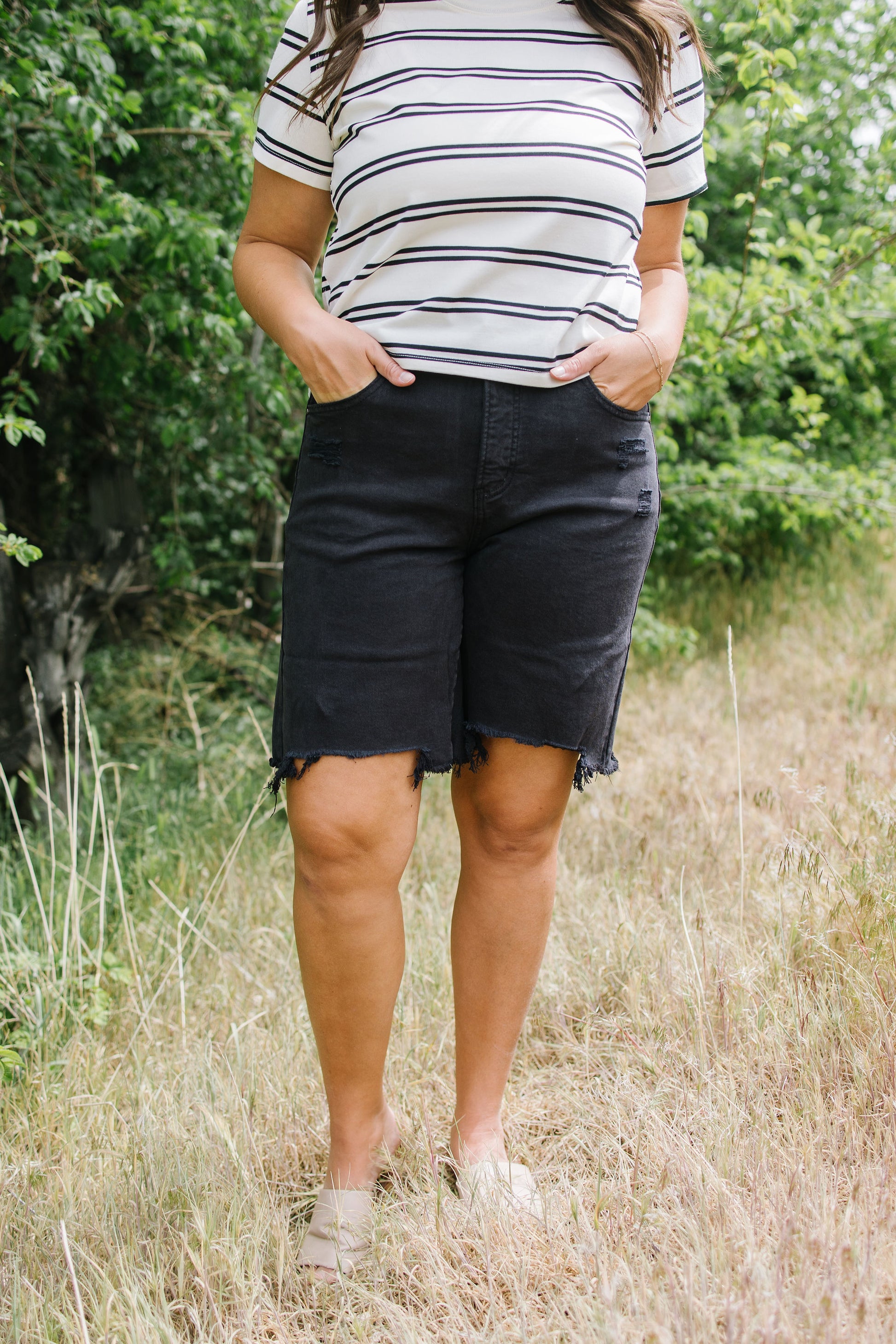 Person wearing a striped shirt and black shorts standing in a grassy field.
