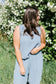 Woman in a light blue jumpsuit standing in front of a white flowering bush.