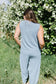 Person wearing a light blue sleeveless top and pants standing in front of a white flowering bush.