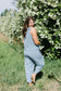 Woman in a light blue jumpsuit standing in front of white flowering bushes.