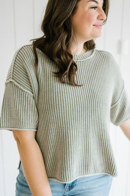 Woman wearing a green knitted sweater and blue jeans against a white background