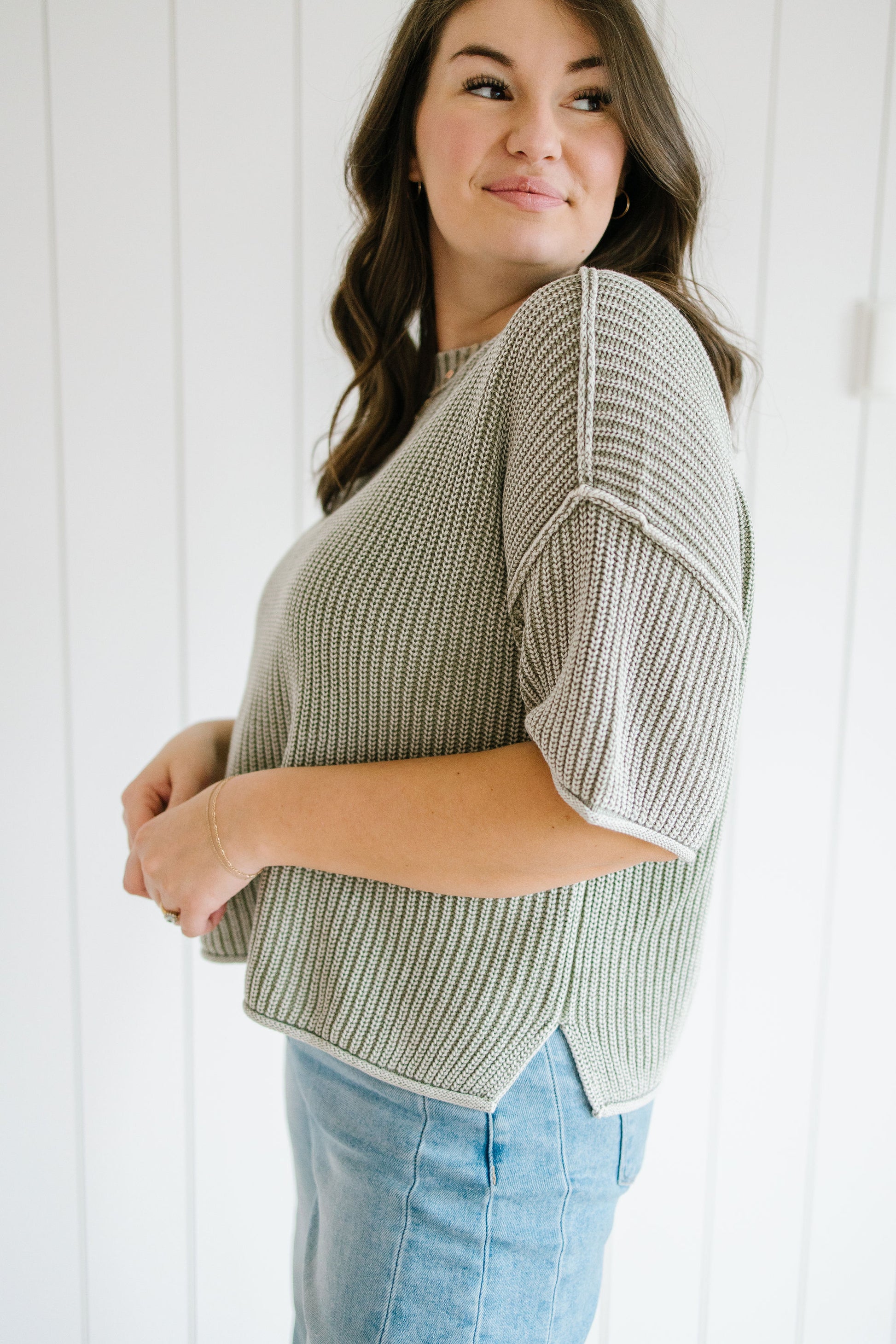 Woman wearing a green and white patterned sweater with light blue jeans against a white background
