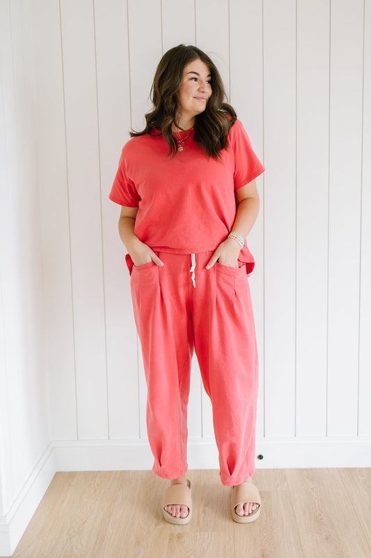 Woman wearing a washed red matching set standing against a white paneled wall.