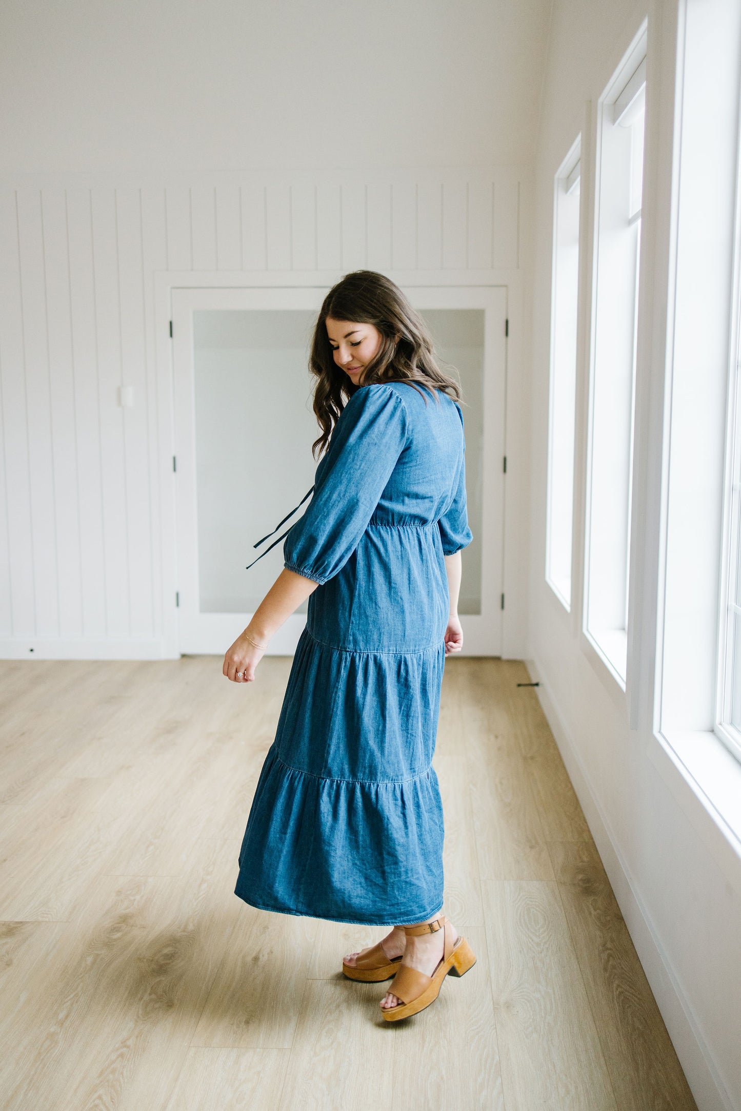 Woman wearing a blue dress standing in a room with large windows.