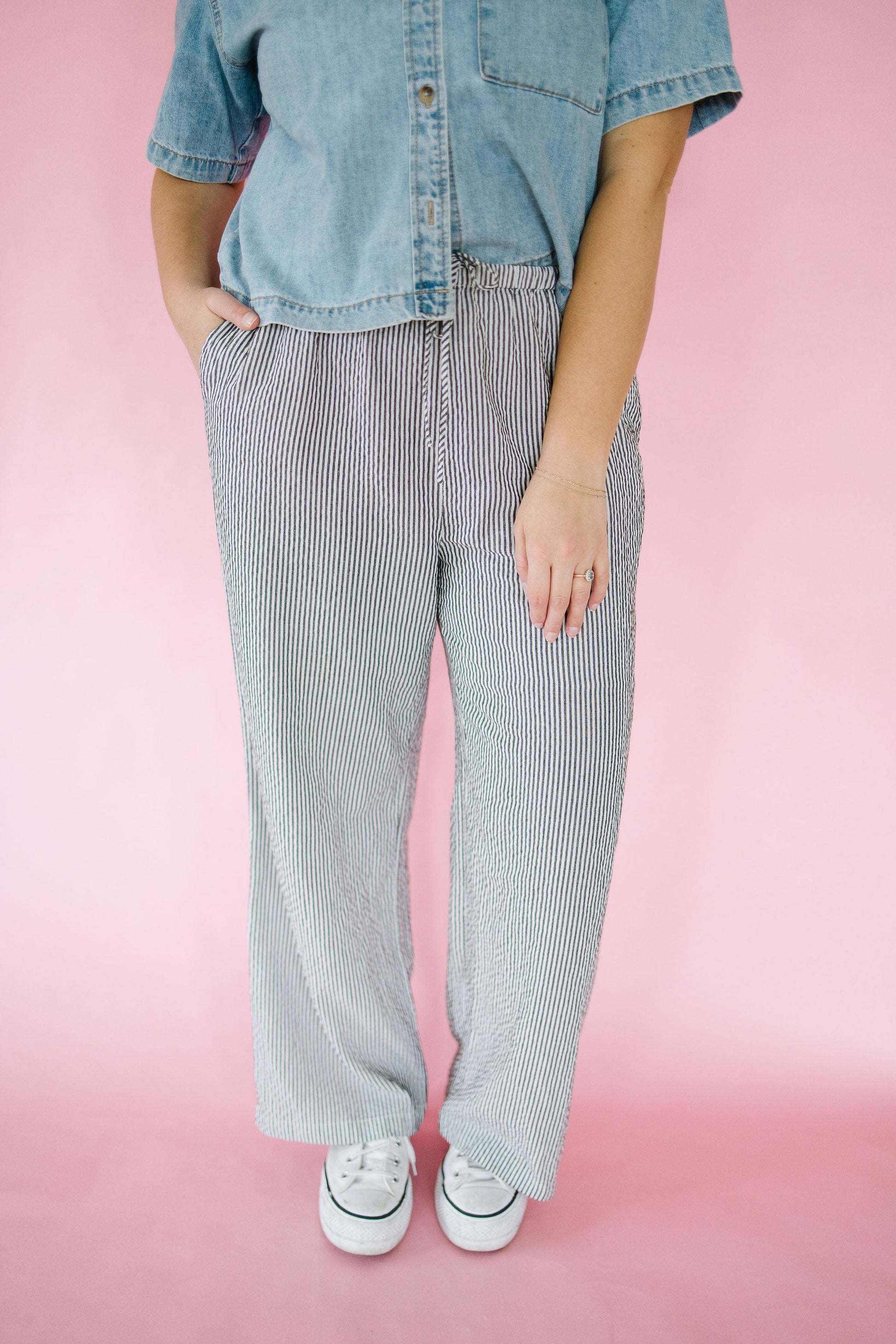 Person wearing a denim shirt and striped pants on a pink background