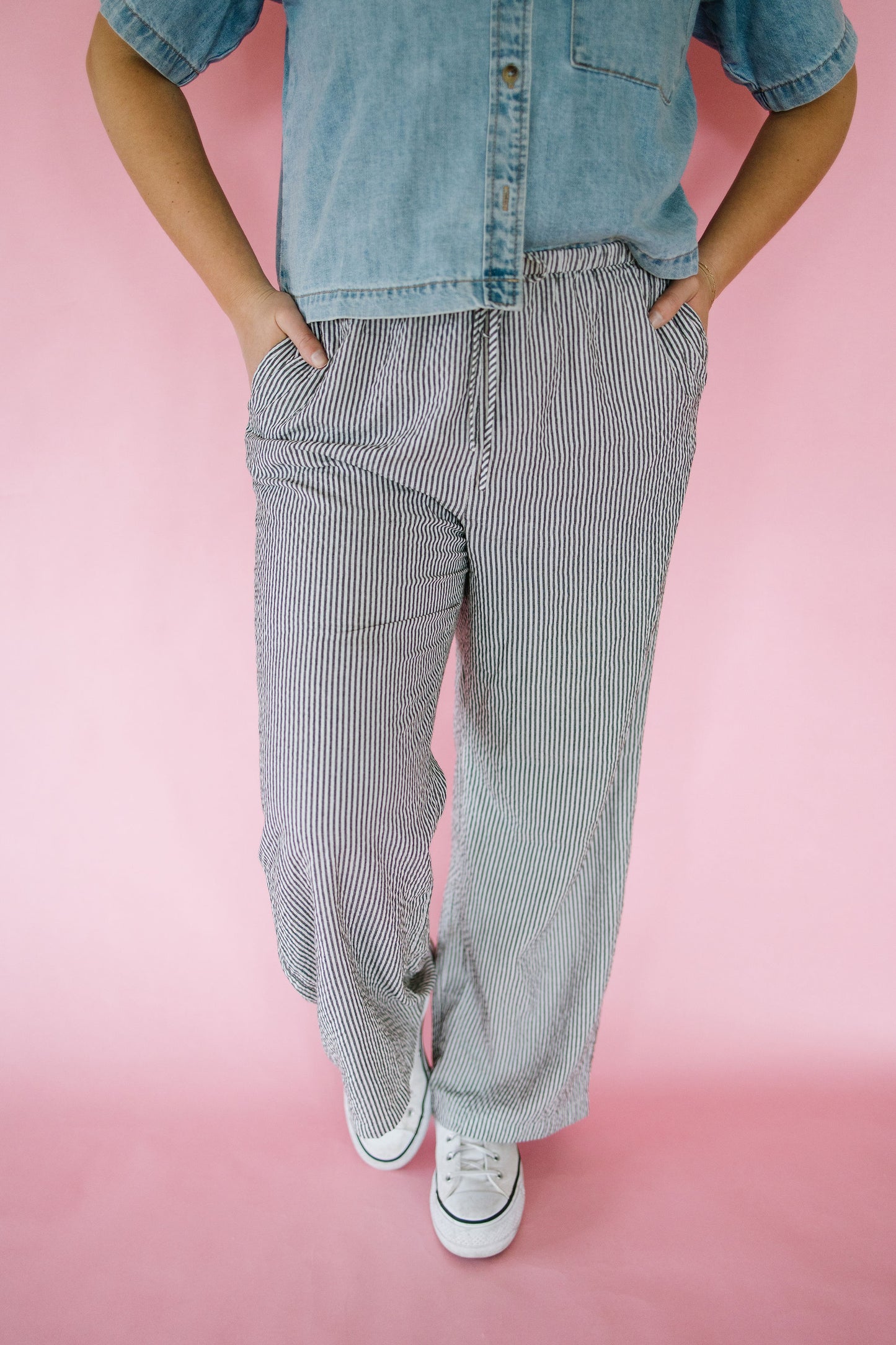 Person wearing a denim shirt and striped pants on a pink background