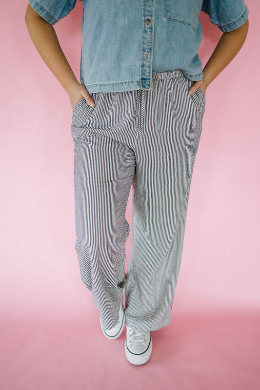 Person wearing a denim shirt and striped pants on a pink background