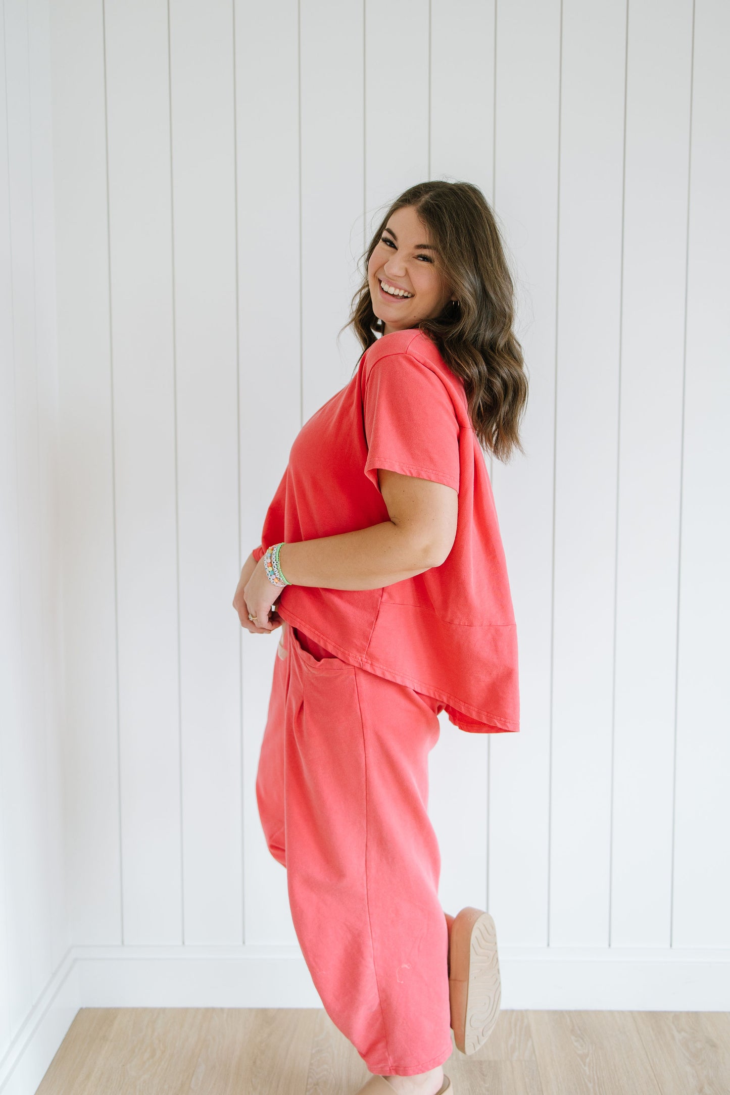 Woman wearing a coral outfit standing against a white paneled wall.