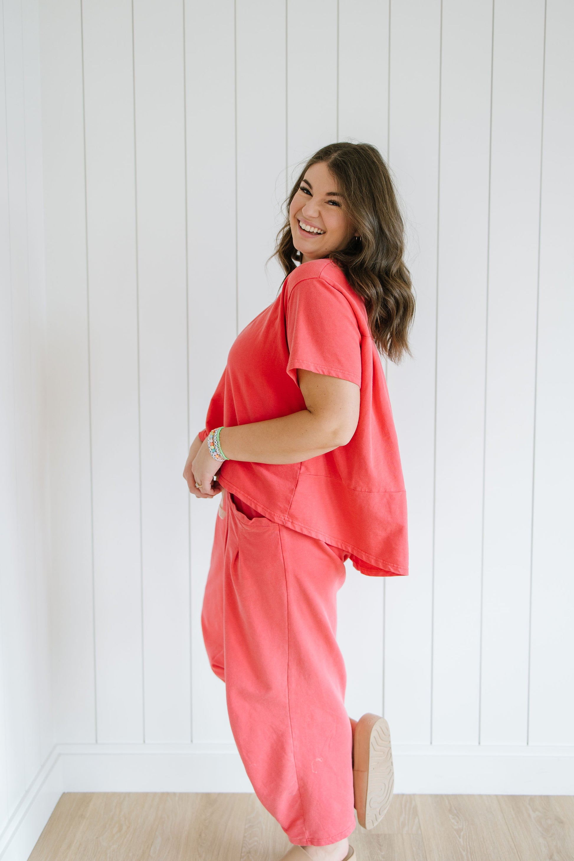 Woman wearing a coral outfit standing against a white paneled wall.