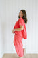 Woman wearing a coral outfit standing against a white paneled wall.
