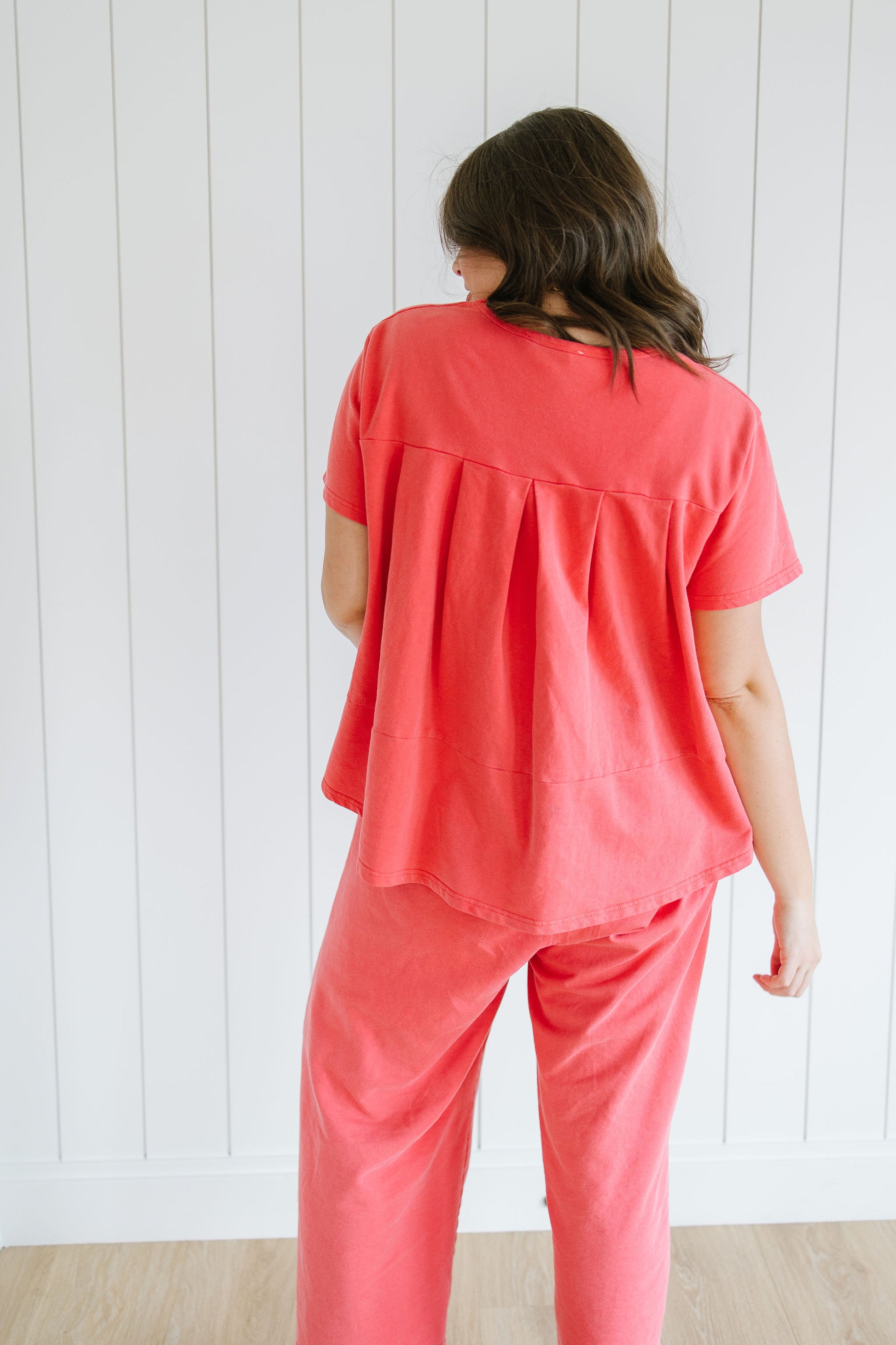 Person wearing a red lounge set standing against a white wooden panel background
