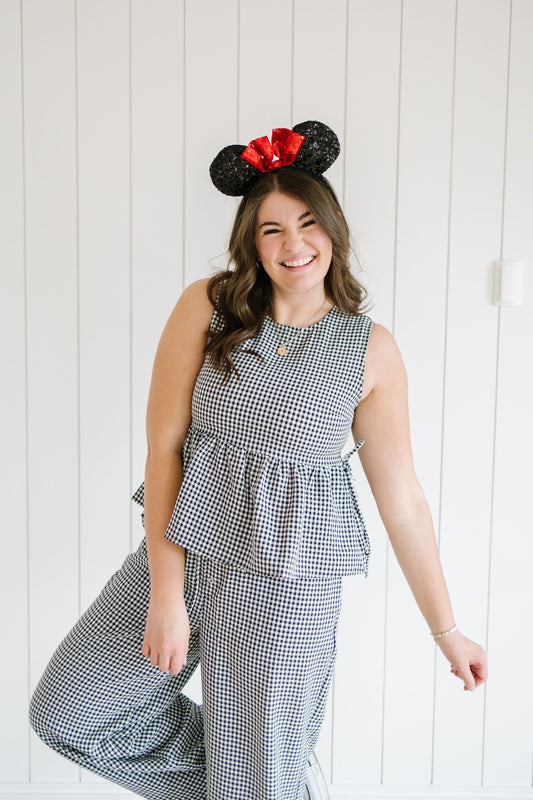 Woman wearing a gingham checkered set and Minnie Mouse ears against a white wooden panel background