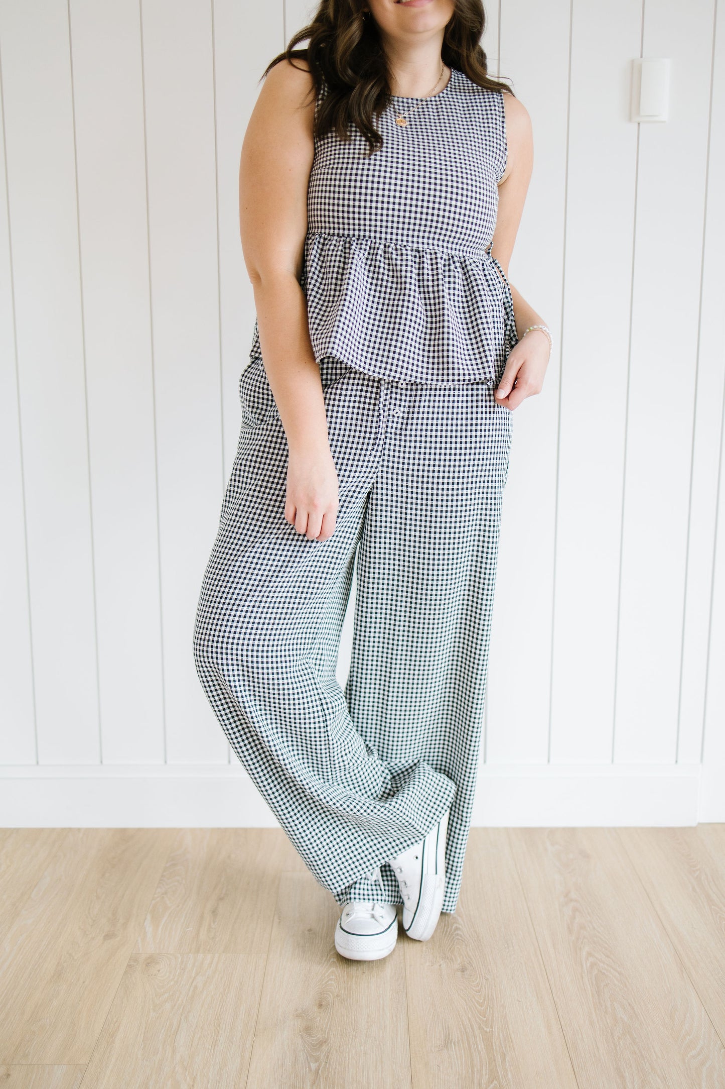 Woman wearing a checkered outfit with a peplum top and wide-leg pants on a wooden floor.