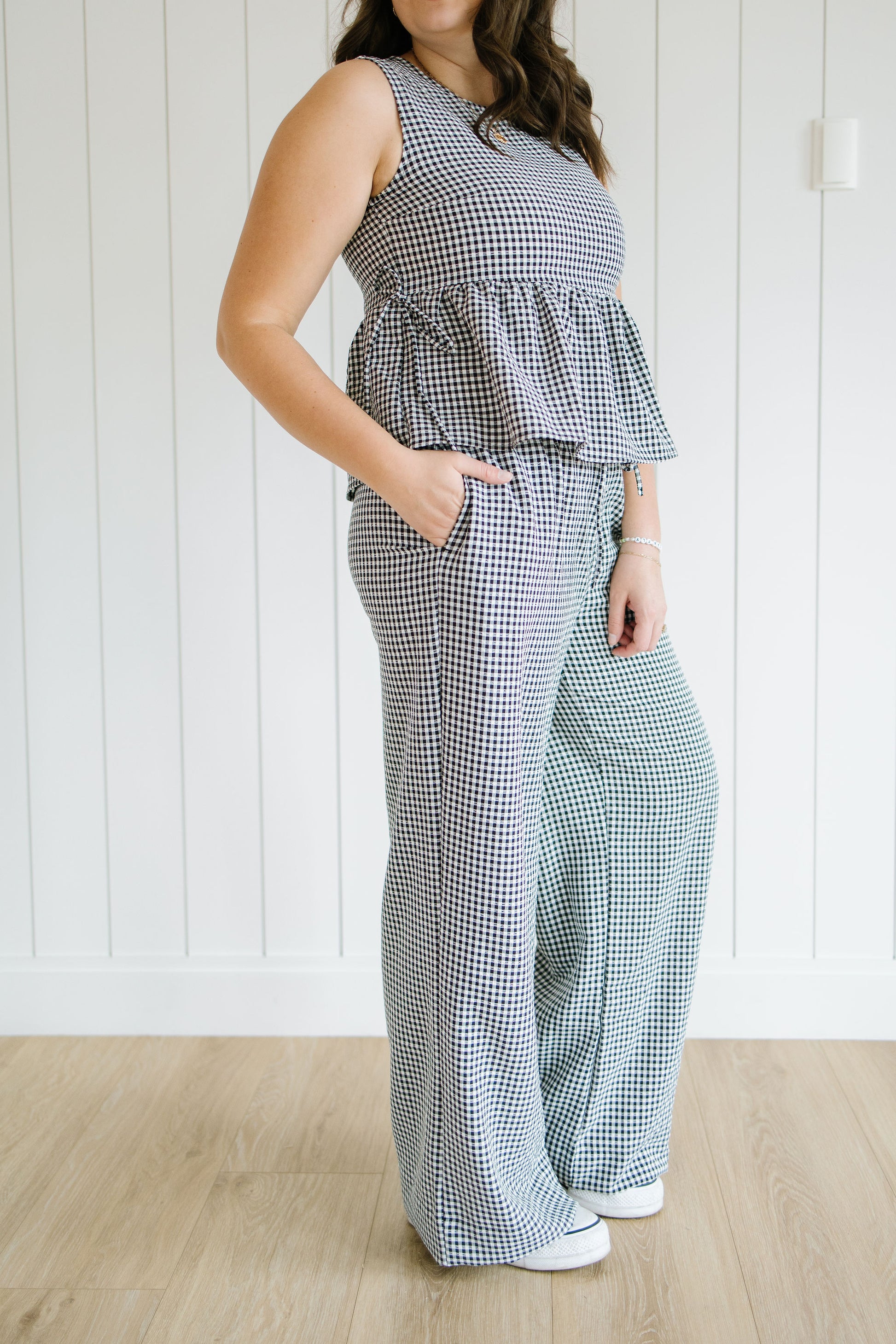 Woman wearing a checkered jumpsuit standing against a white paneled wall.