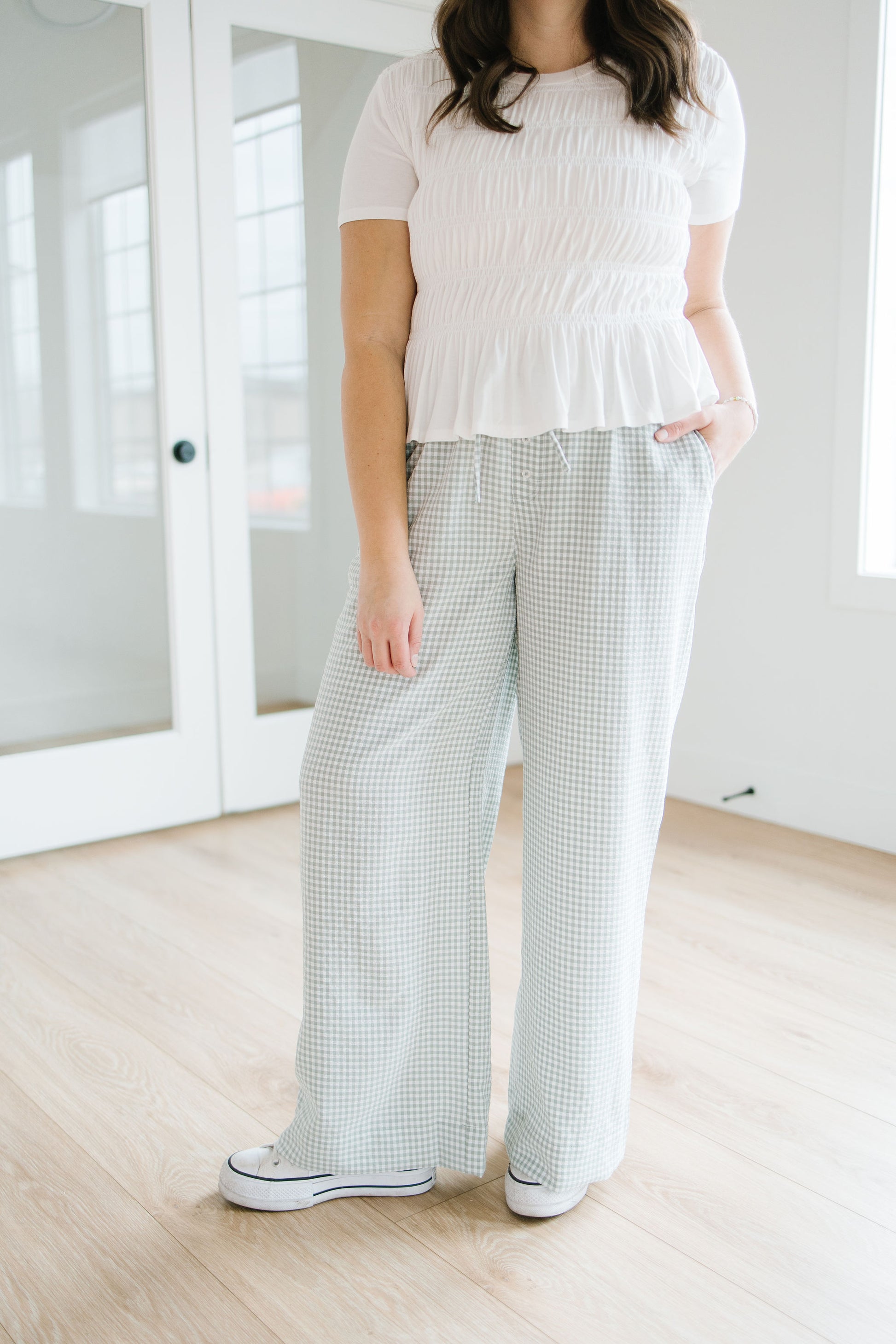 Person wearing a white top and checkered pants in a minimal indoor setting