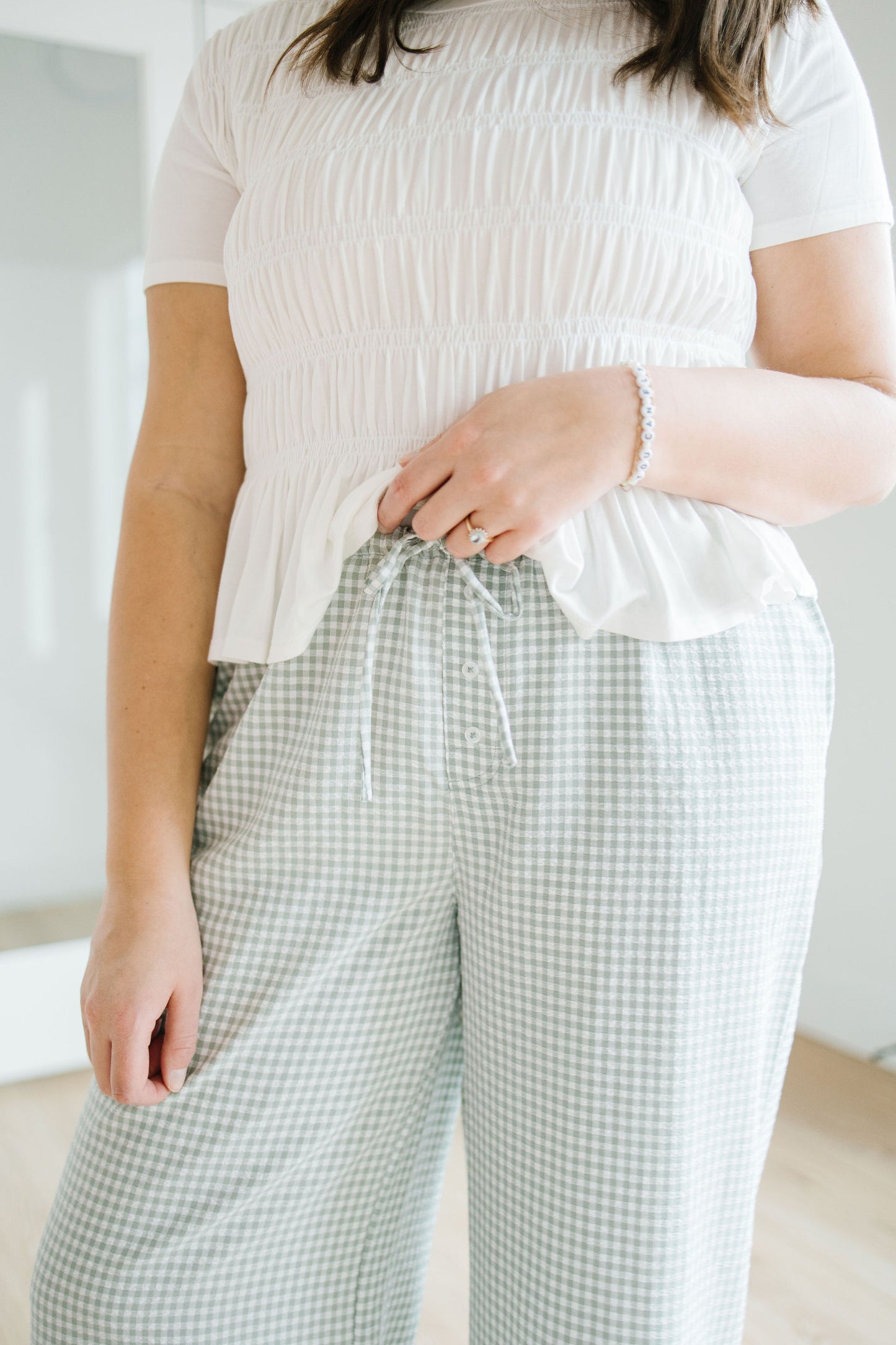 Person wearing a white textured top and green checkered pants in a minimal indoor setting