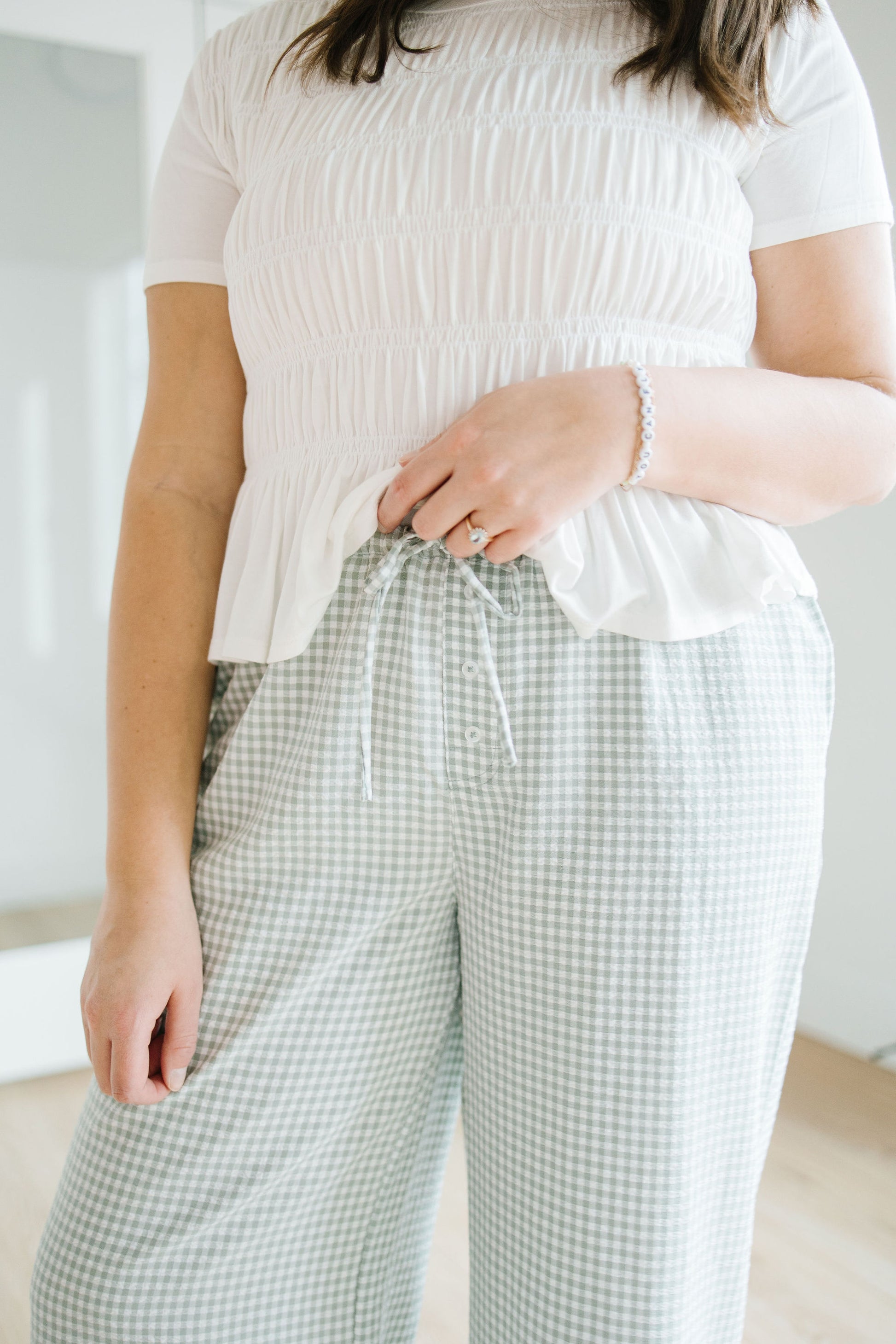 Person wearing a white textured top and green checkered pants in a minimal indoor setting