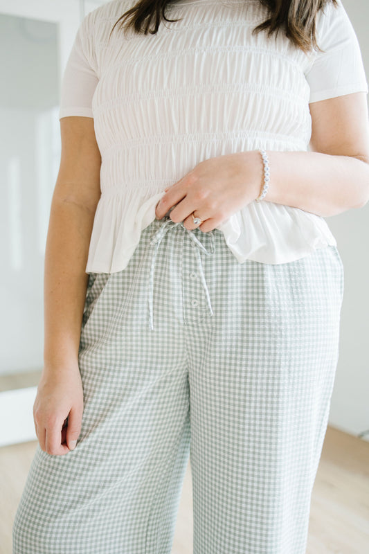 Person wearing a white textured top and green checkered pants in a minimal indoor setting