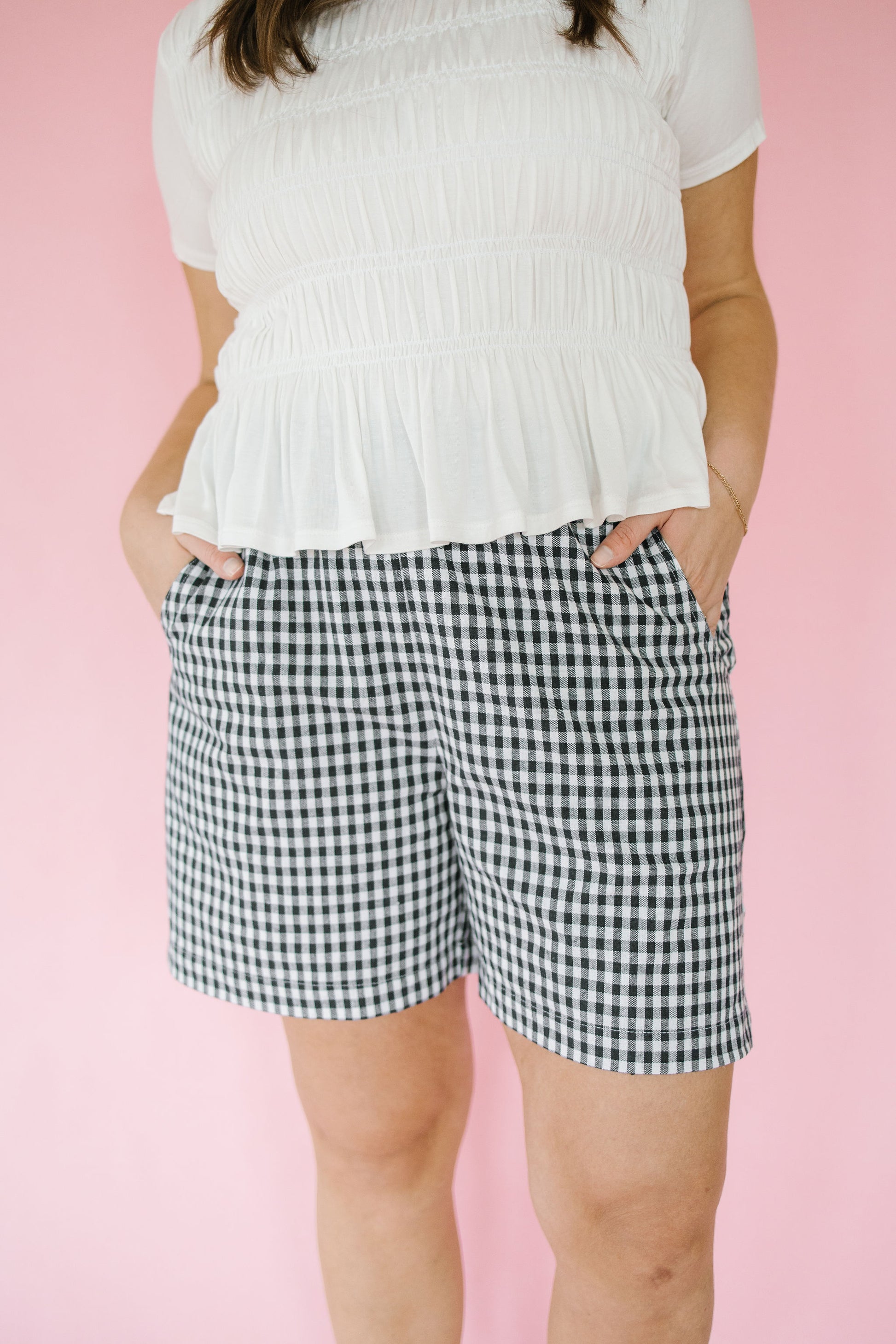 Person wearing a white top and navy and white checkered shorts on a pink background