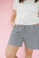 Person wearing a white top and black and white checkered shorts on a pink background