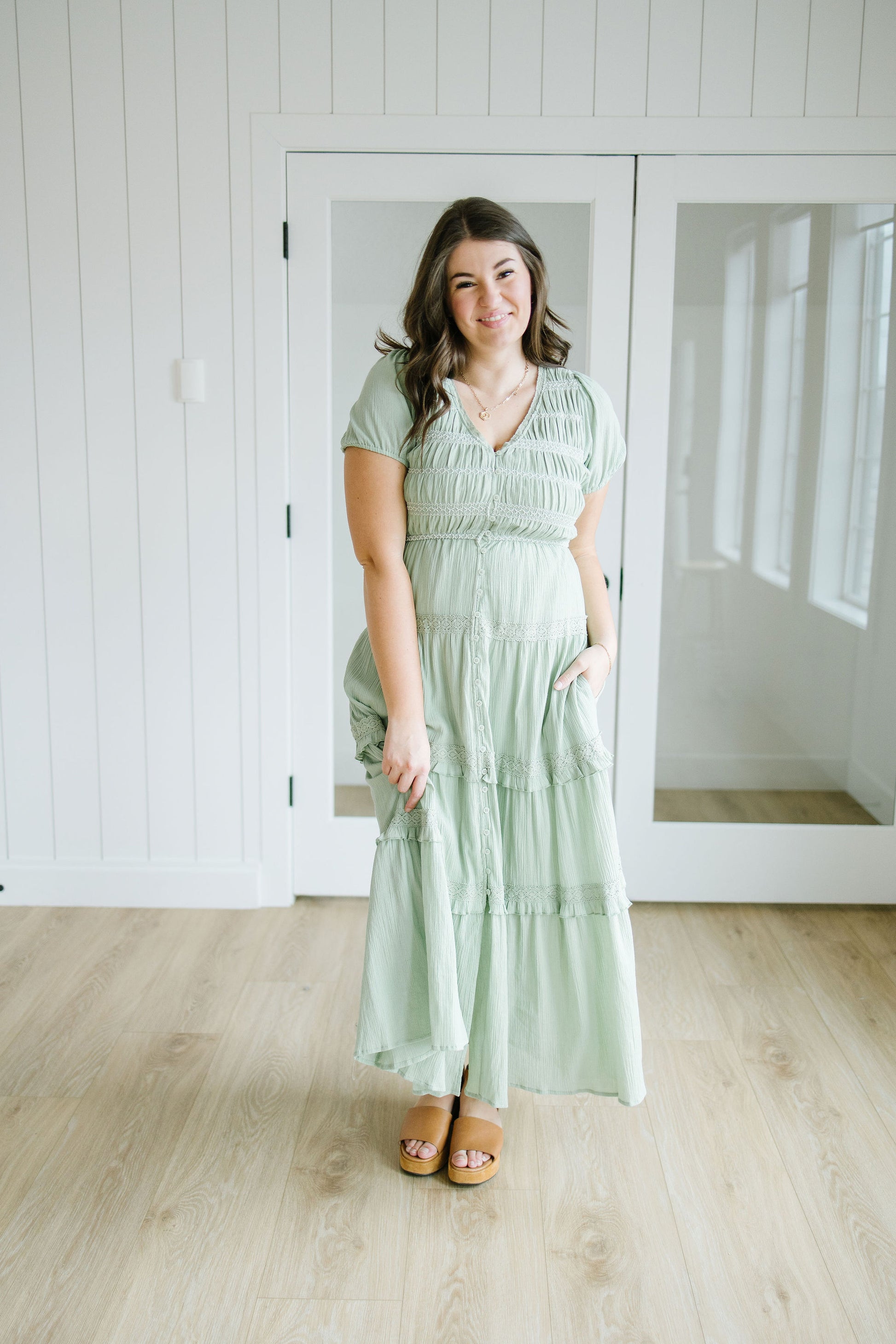 Woman wearing a light green dress standing in a room with white walls and wooden flooring.