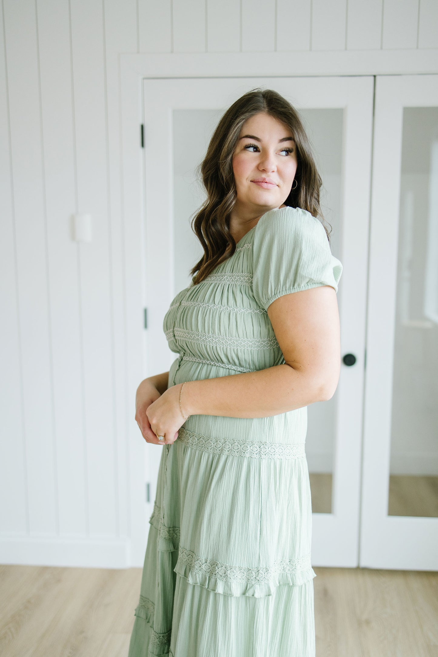 Woman wearing a light green dress standing in a room with white walls and doors.
