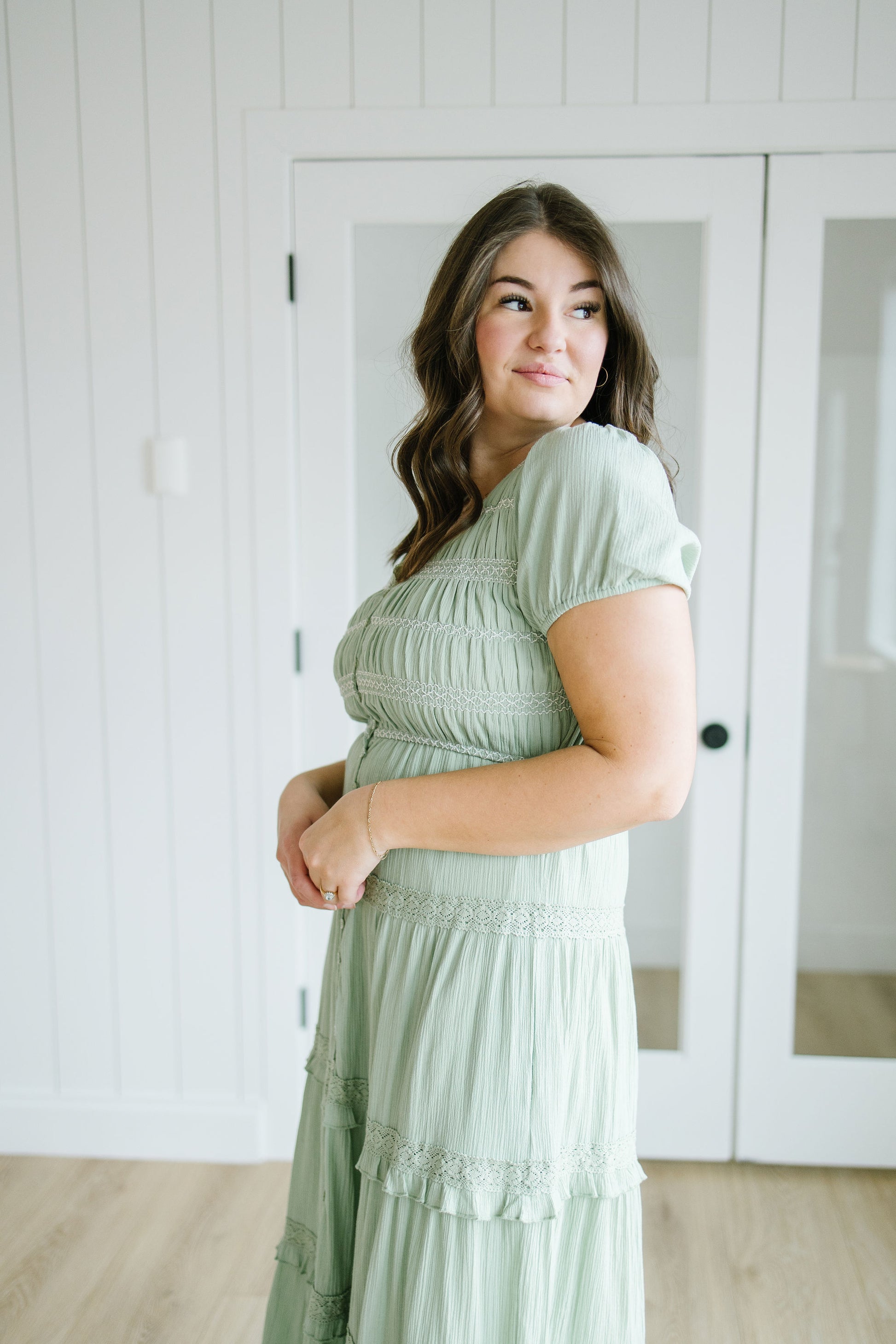 Woman wearing a light green dress standing in a room with white walls and doors.