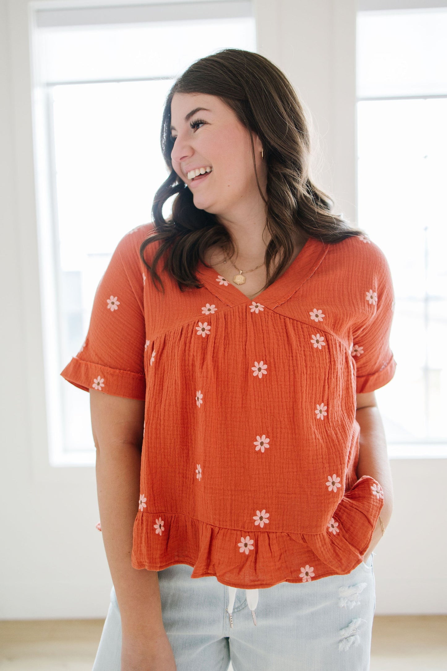 Woman wearing an orange blouse with embroidered white floral patterns in a bright room.