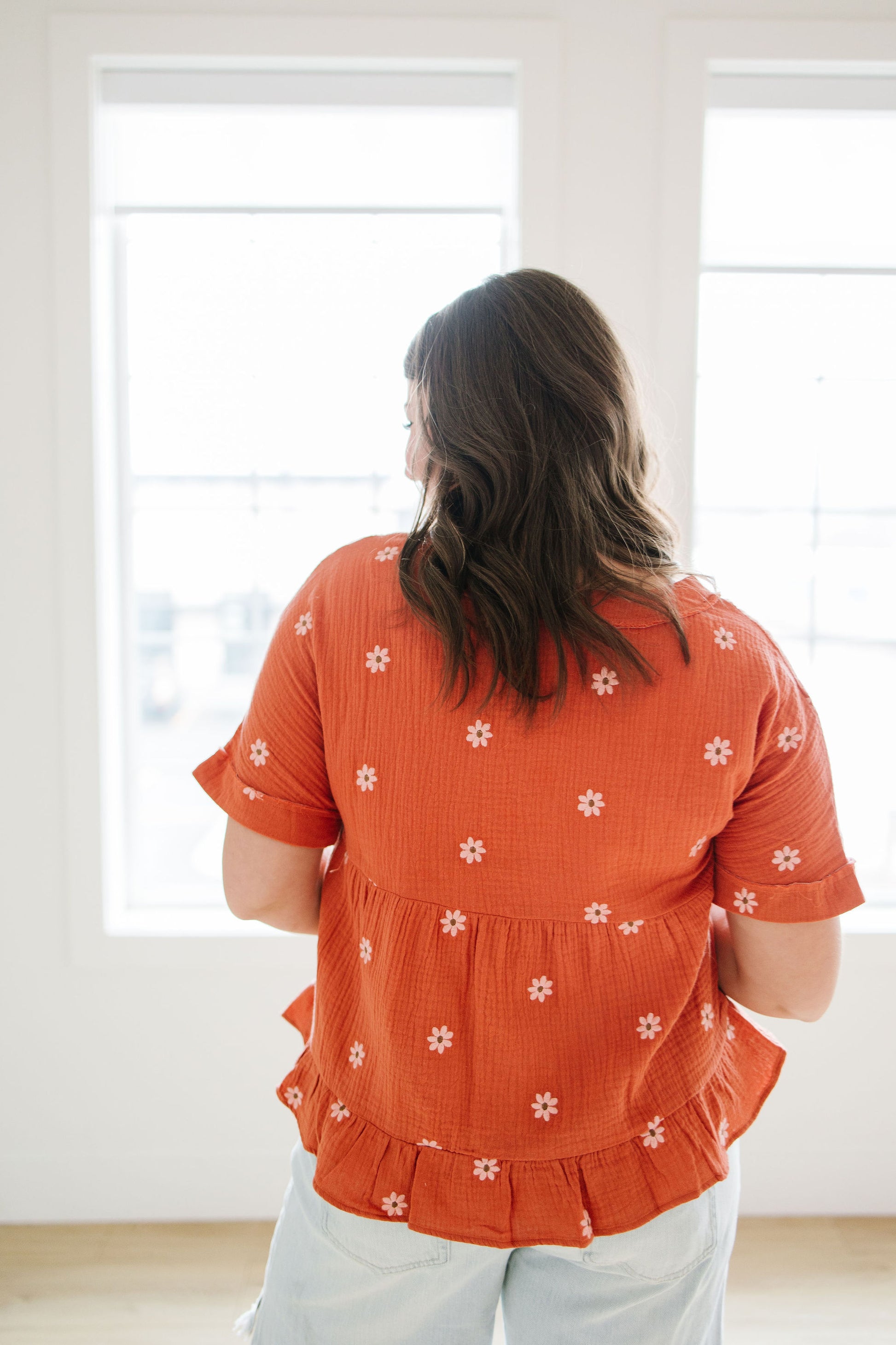 Person wearing an orange floral blouse standing in a room with white walls and windows.
