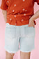 Person wearing an orange top with white floral patterns and light blue denim shorts on a pink background