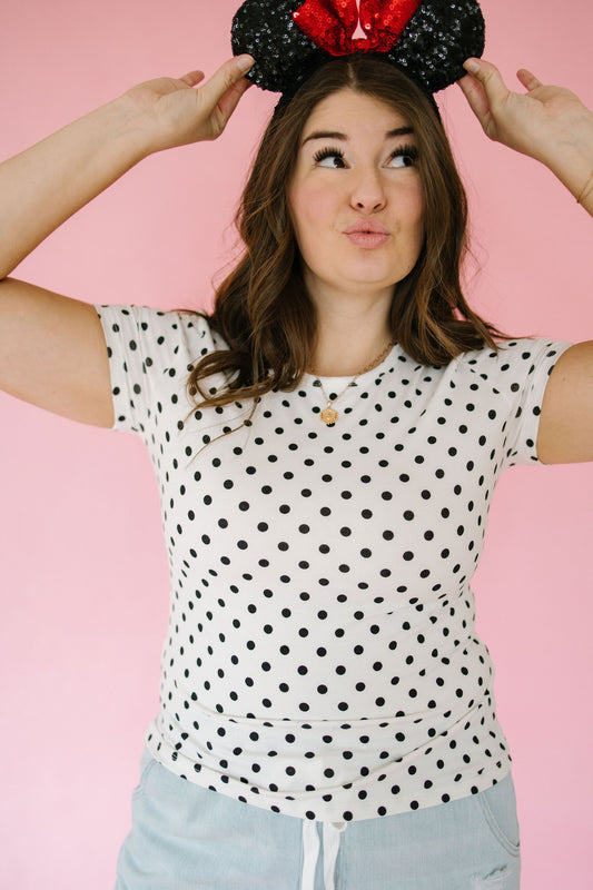 Person wearing a polka dot shirt and black and red mouse ears against a pink background