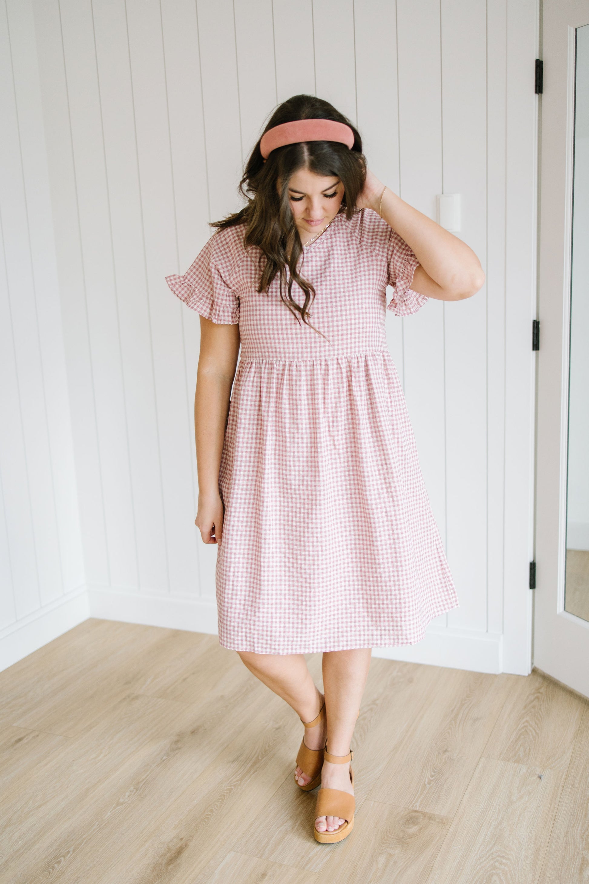 Woman wearing a pink checkered dress with a headband indoors.